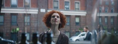 a woman with red hair standing in front of a building