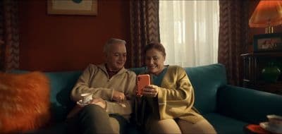 a man and woman sitting on a couch looking at a cell phone
