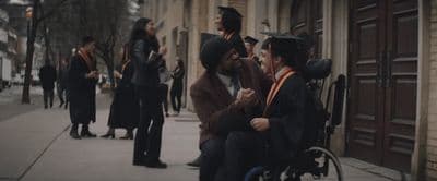 a man in a wheelchair talking to a woman in a graduation gown
