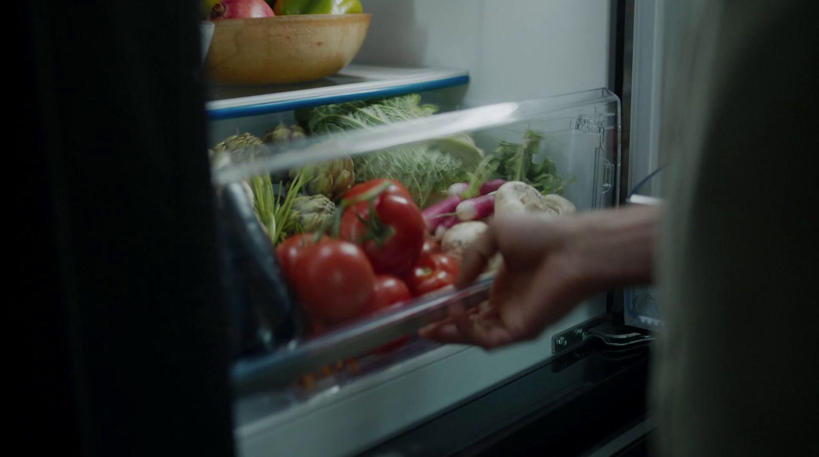 a person reaching into an open refrigerator filled with vegetables