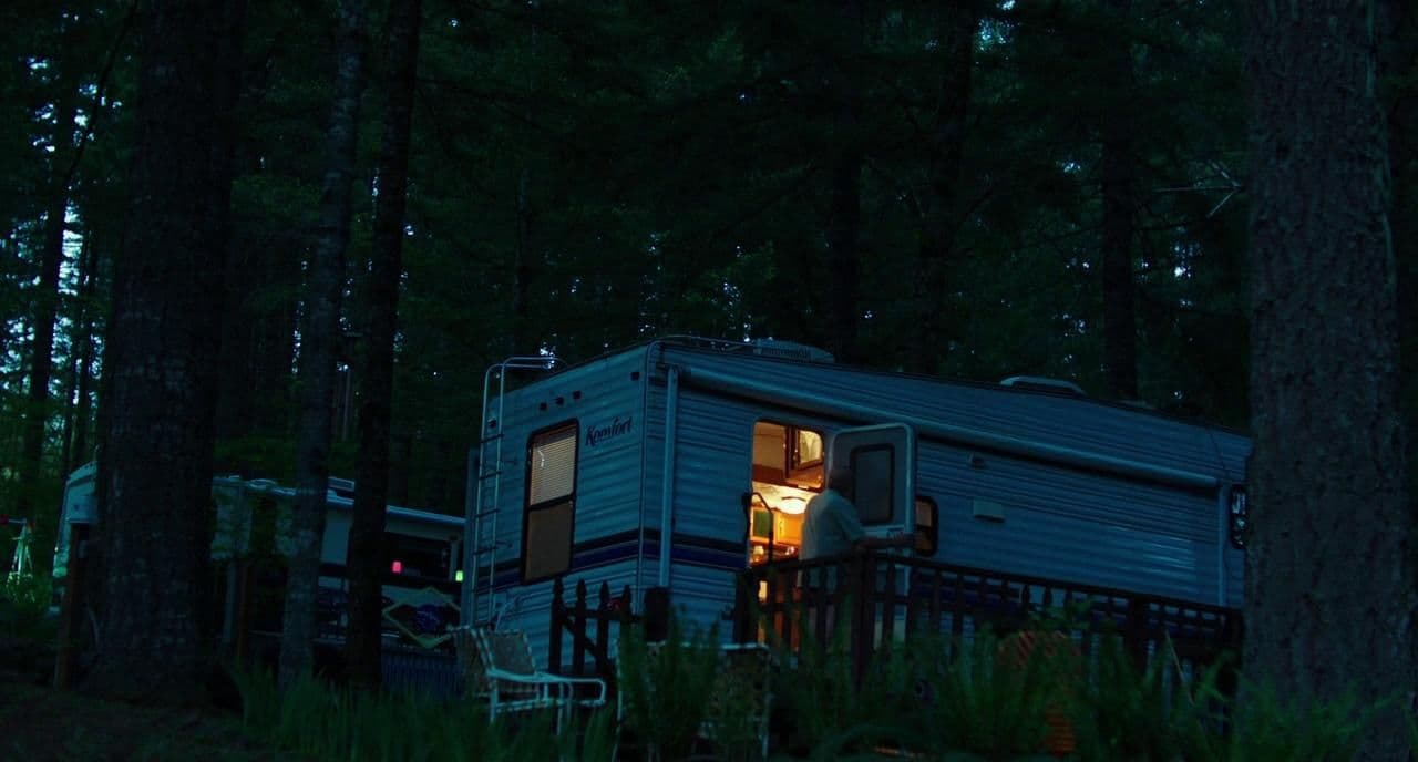 a person standing outside of a blue trailer in the woods