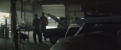 a couple of men standing next to a car in a garage