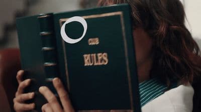 a woman holding a green book with the word rules on it