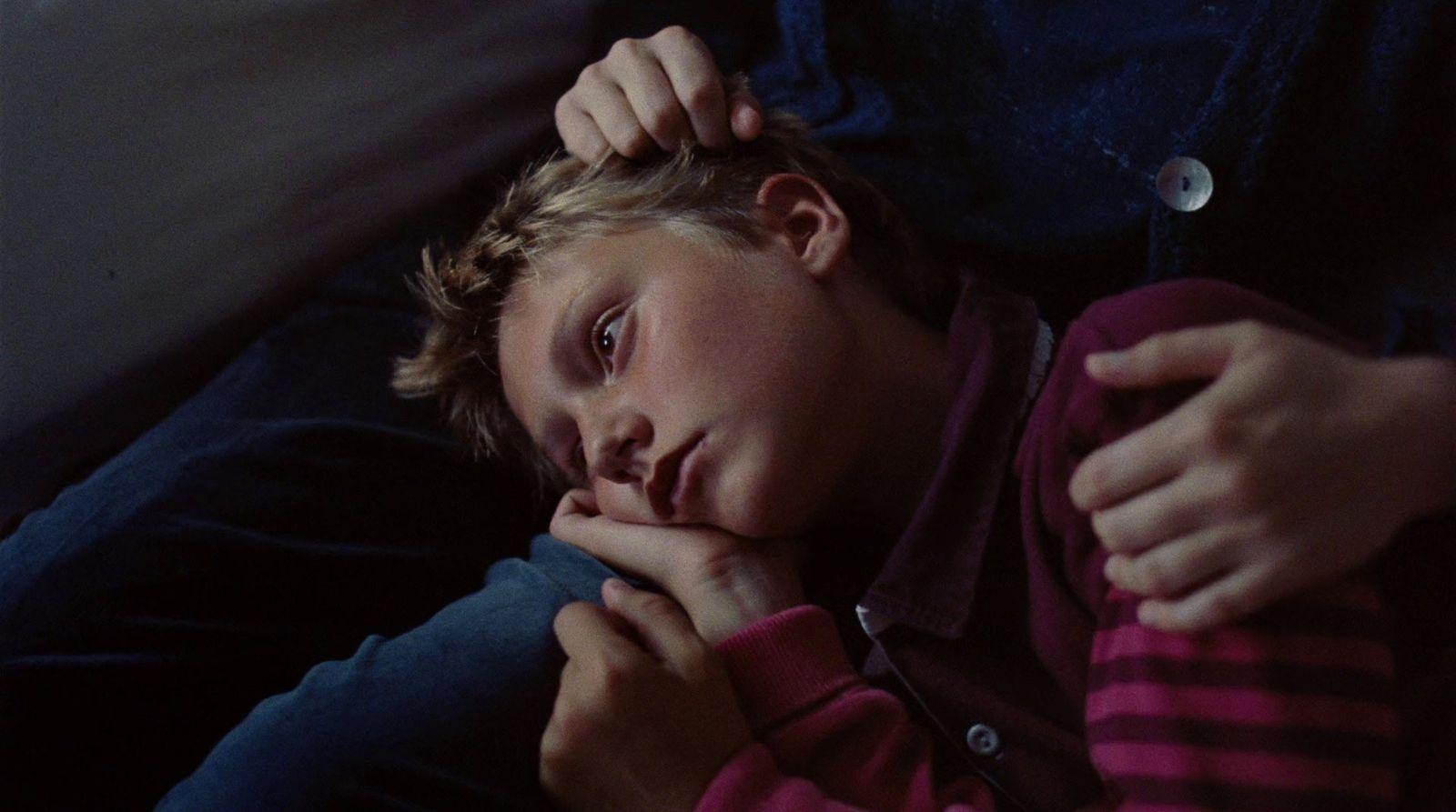 a young boy sitting on a couch with his hand on his chin