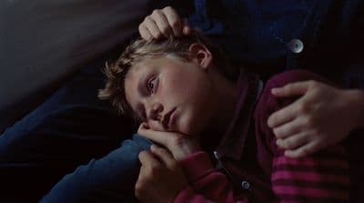 a young boy sitting on a couch with his hand on his chin