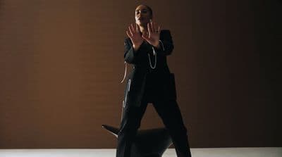 a woman in a black suit standing in front of a brown wall