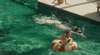 a woman riding a raft in a pool next to a dog