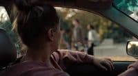a woman sitting in a car with her hand on the steering wheel
