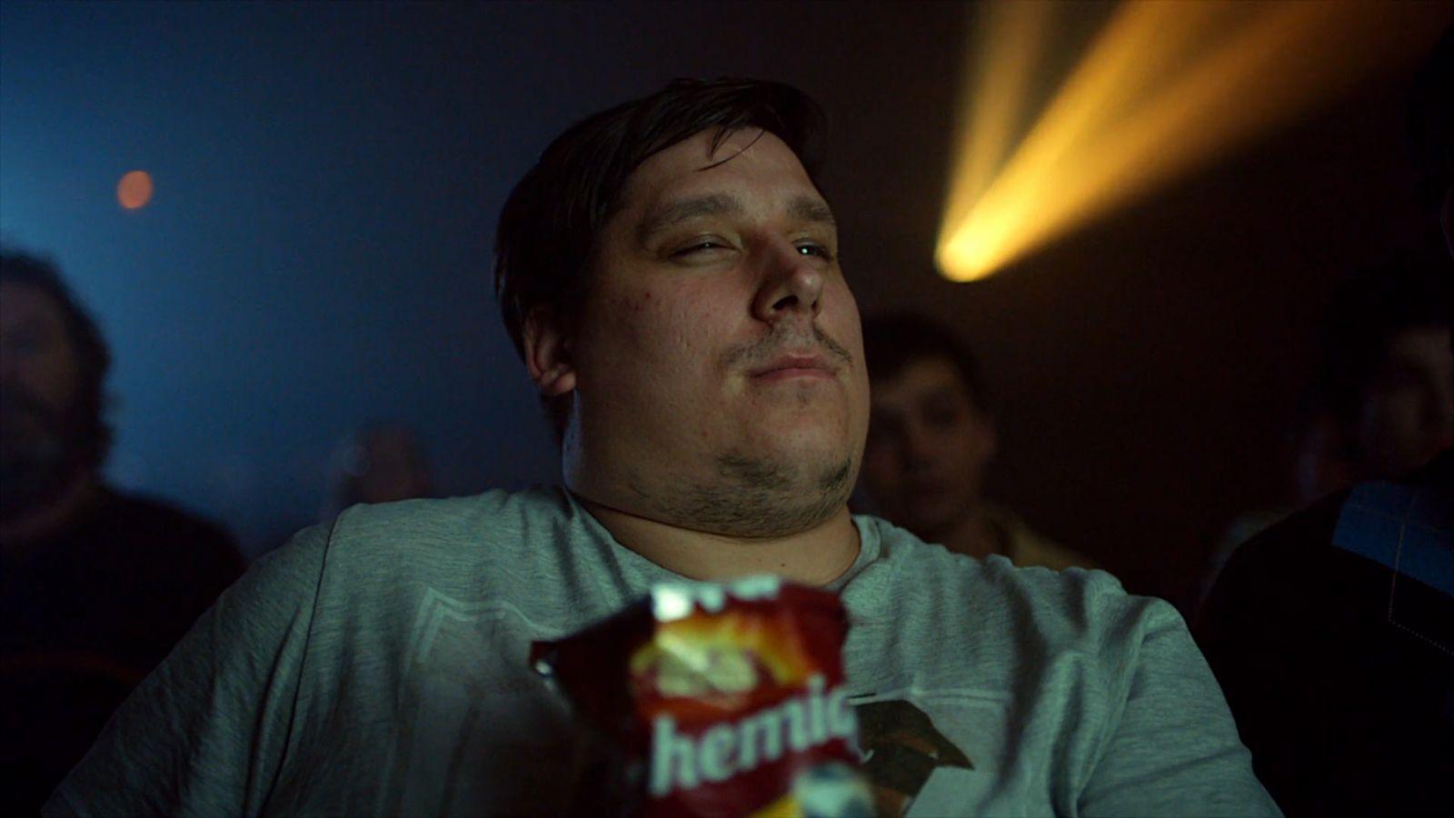a man sitting in a dark room holding a bag of chips