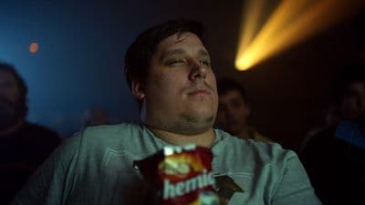 a man sitting in a dark room holding a bag of chips