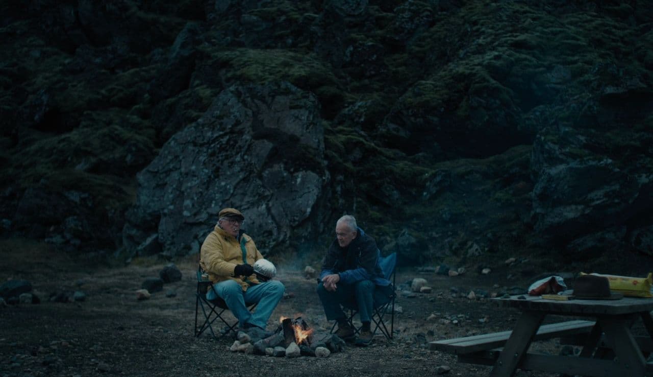 a couple of men sitting next to each other near a fire