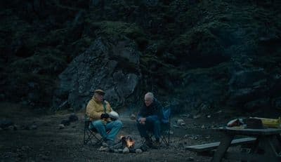 a couple of men sitting next to each other near a fire