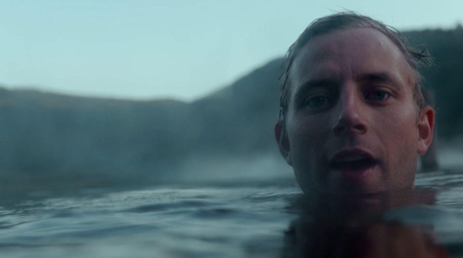 a man swimming in a lake with mountains in the background