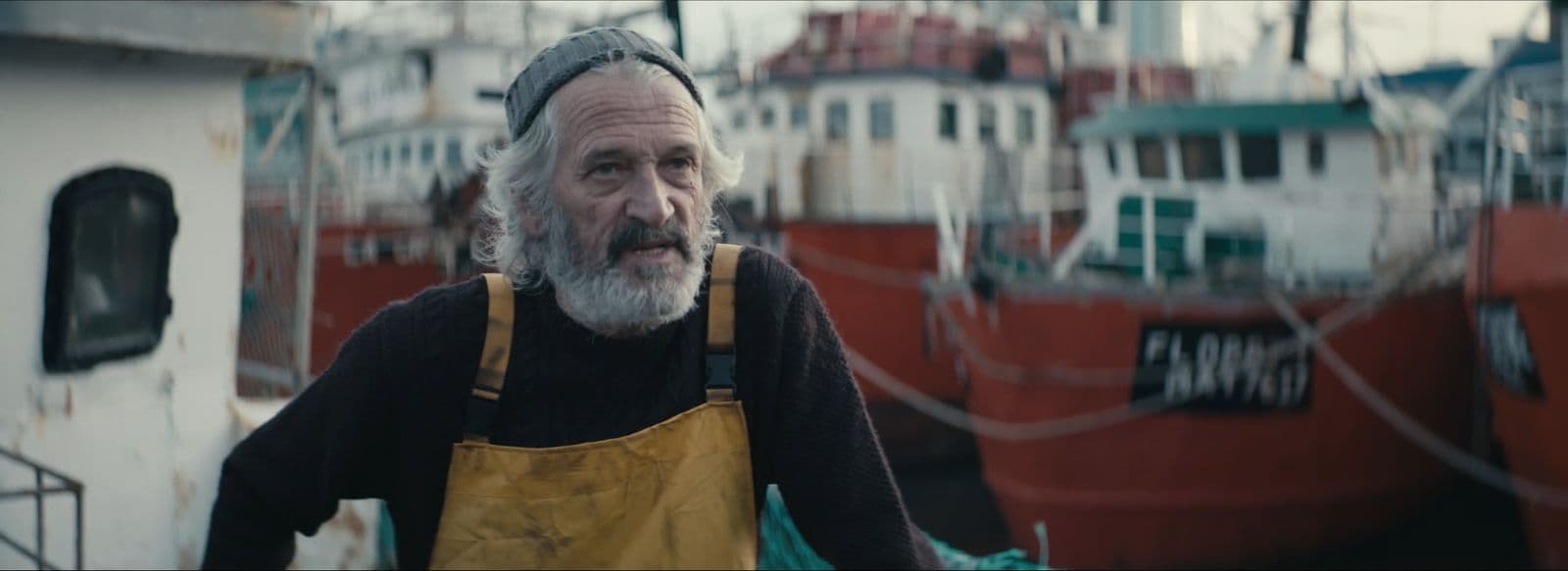 a man with a beard and a yellow apron standing in front of a boat