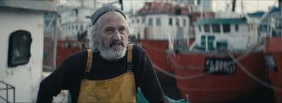 a man with a beard and a yellow apron standing in front of a boat