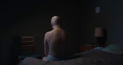 a naked man sitting on a bed in a dark room