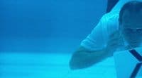 a man in a white shirt and sunglasses swimming in a pool