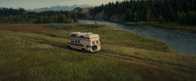 an rv parked in a grassy field next to a river