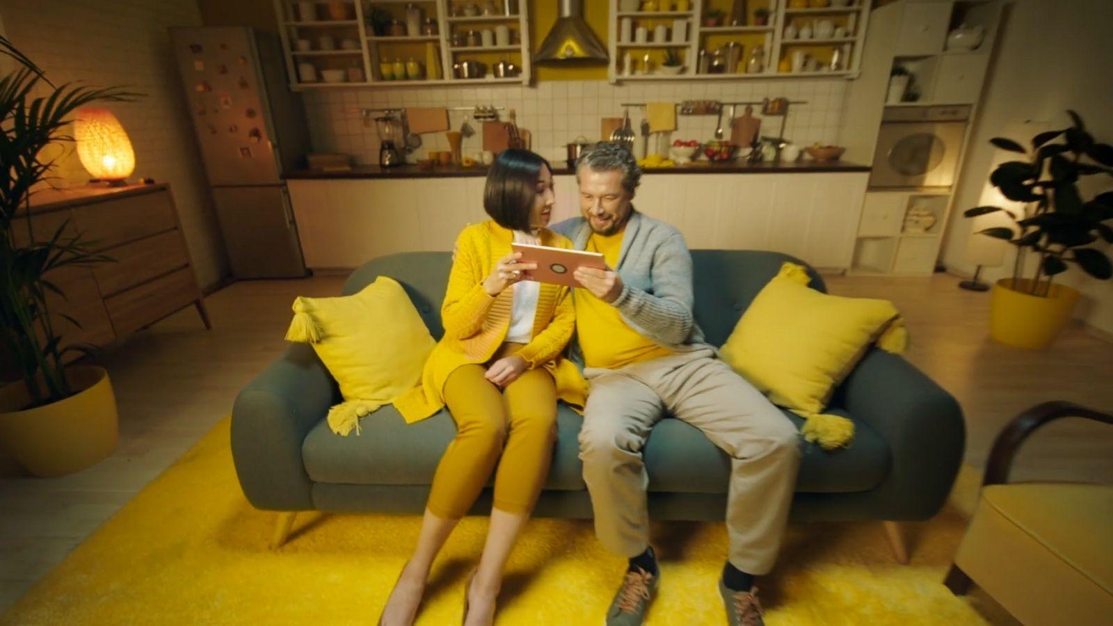 a man and woman sitting on a couch looking at a tablet