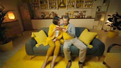 a man and woman sitting on a couch looking at a tablet