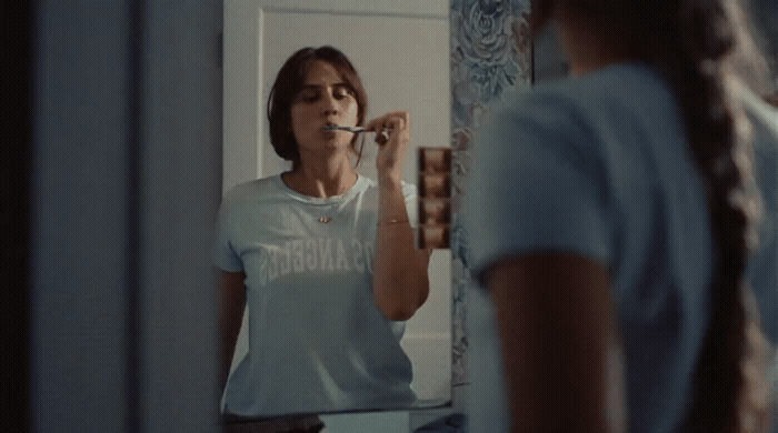 a woman standing in front of a mirror brushing her teeth