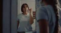 a woman standing in front of a mirror brushing her teeth