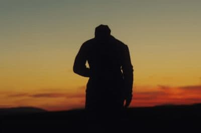 a silhouette of a man standing in front of a sunset