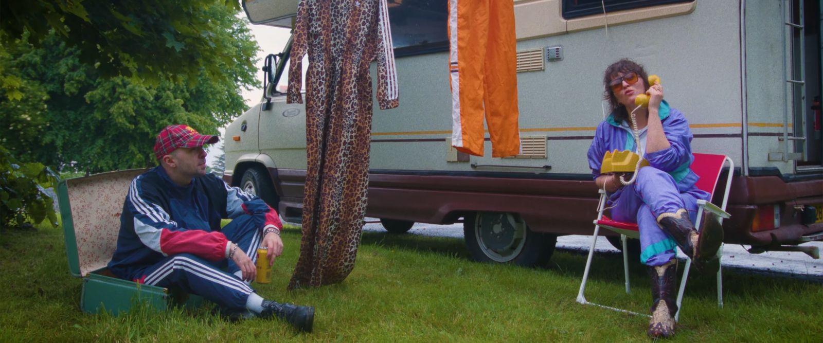 a man and a woman sitting in chairs in front of a camper