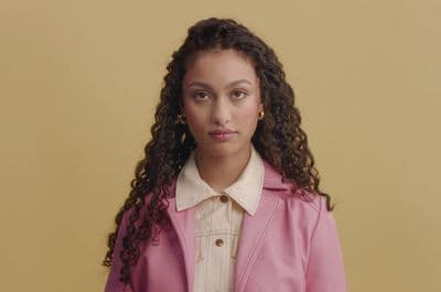 a young woman with curly hair wearing a pink coat