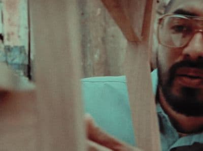 a man wearing glasses looking through a piece of wood