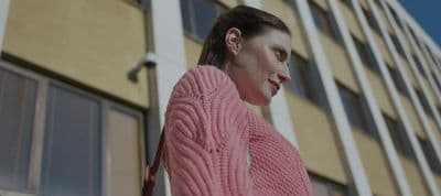 a woman in a pink sweater standing in front of a building