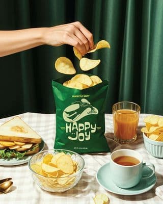 a person holding a bag of chips over a table full of food