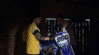 a man standing next to a man on a dirt bike