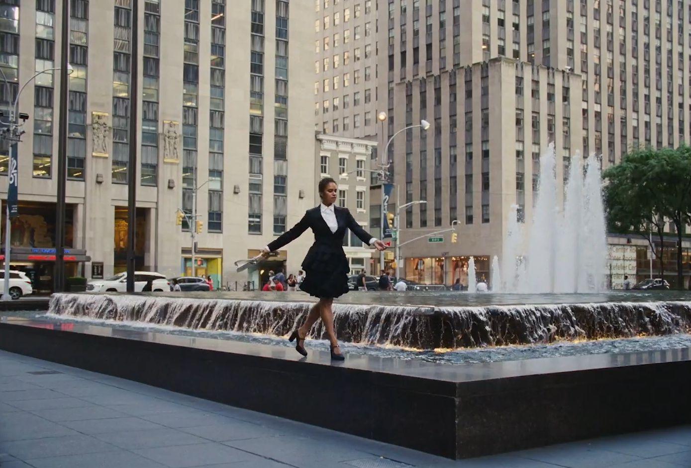 a woman in a black dress standing in front of a fountain