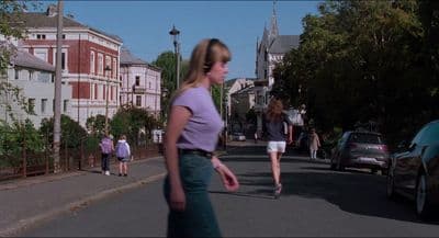 a woman walking down a street next to parked cars