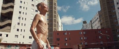 a man without a shirt standing in front of a tall building