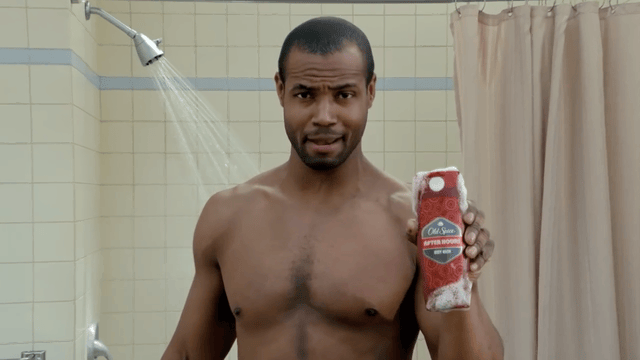 a shirtless man holding a bottle of soap in a bathroom