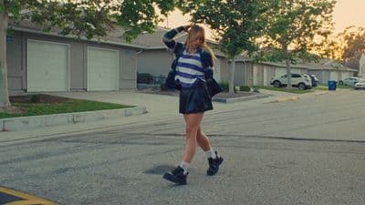 a woman walking across a street next to a parking lot