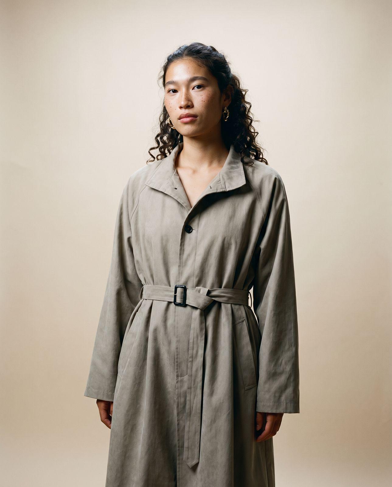 a woman in a trench coat standing in front of a wall