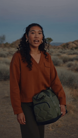 a woman in a brown sweater is holding a green bag