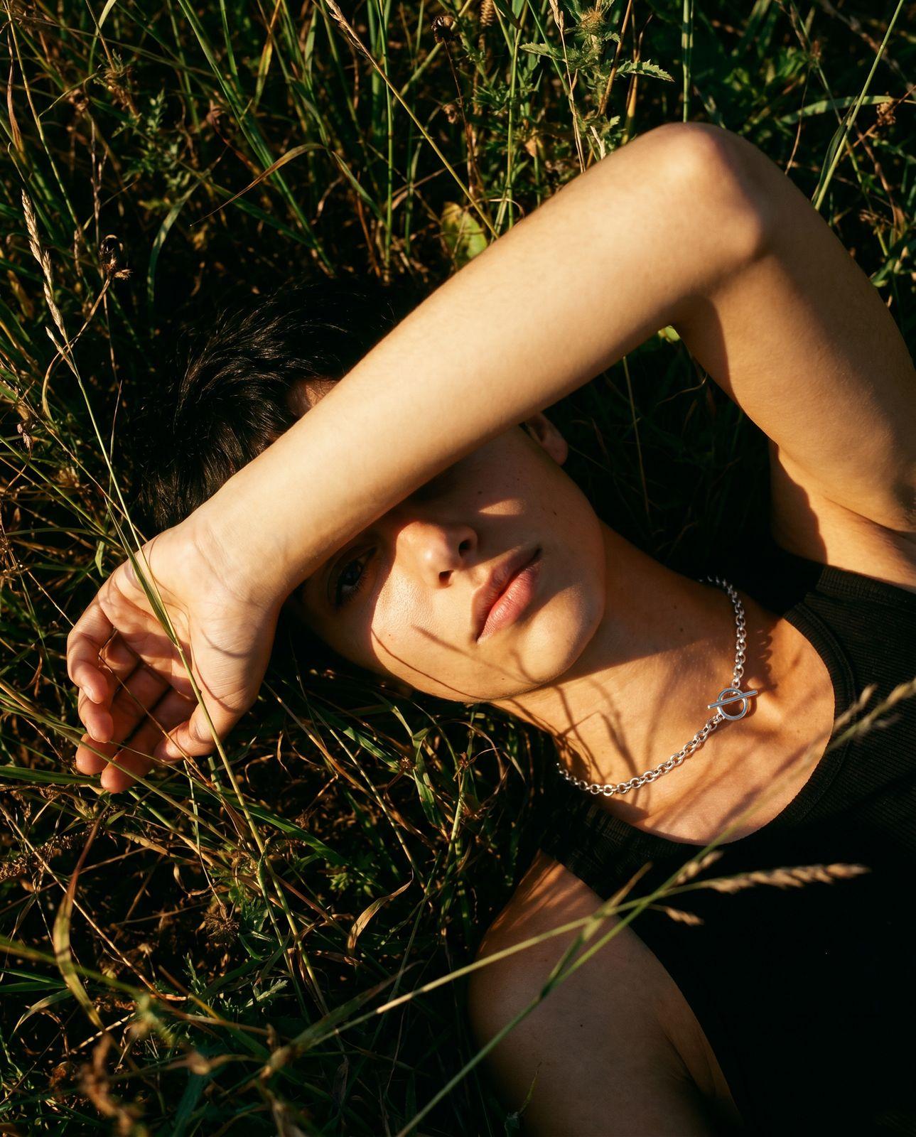 a woman laying in the grass wearing a necklace