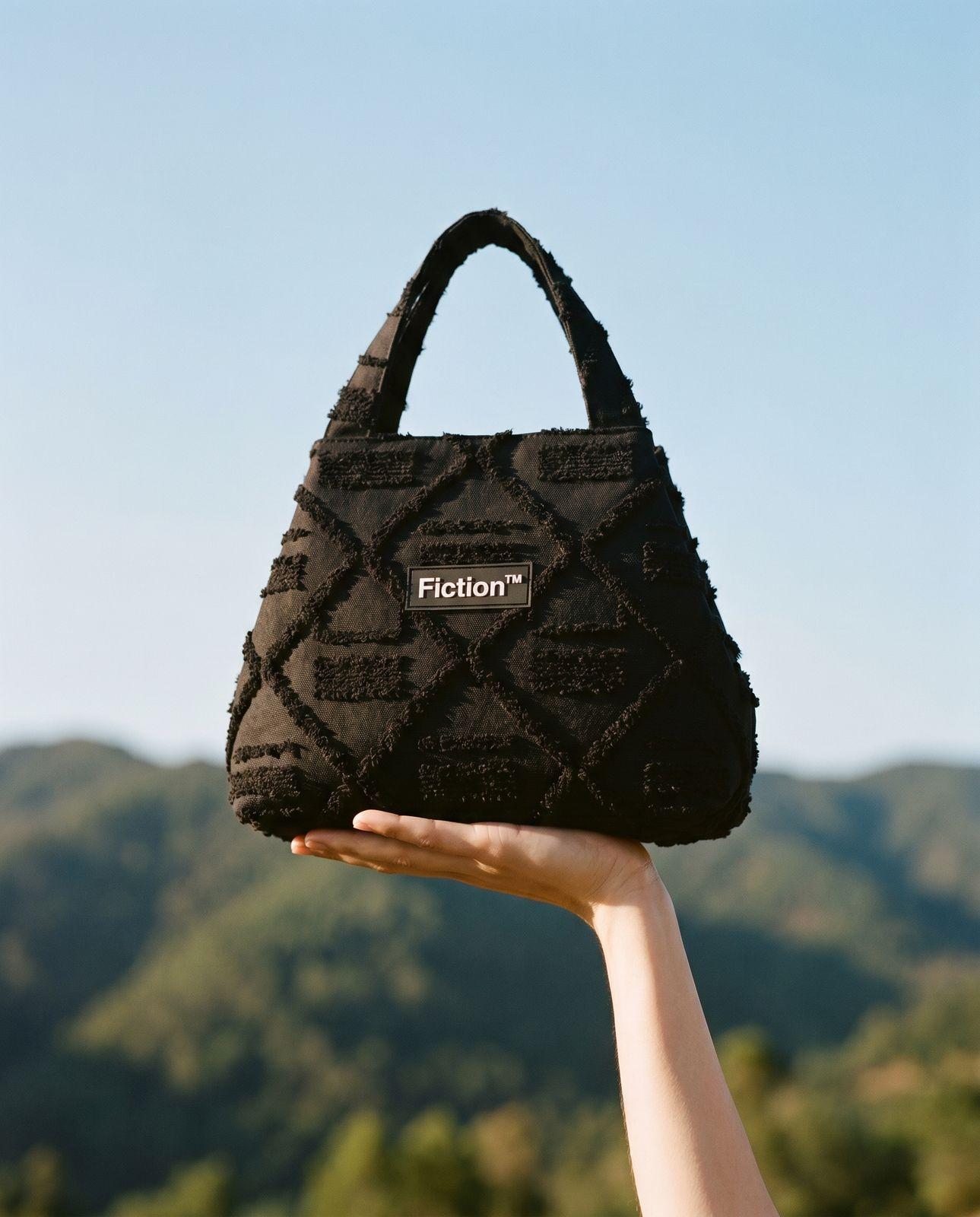 a hand holding a black purse with the word fiction on it