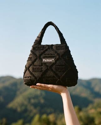 a hand holding a black purse with the word fiction on it