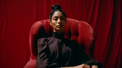 a woman sitting in a red chair in front of a red curtain