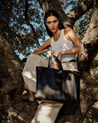 a woman sitting in a tree holding a black bag