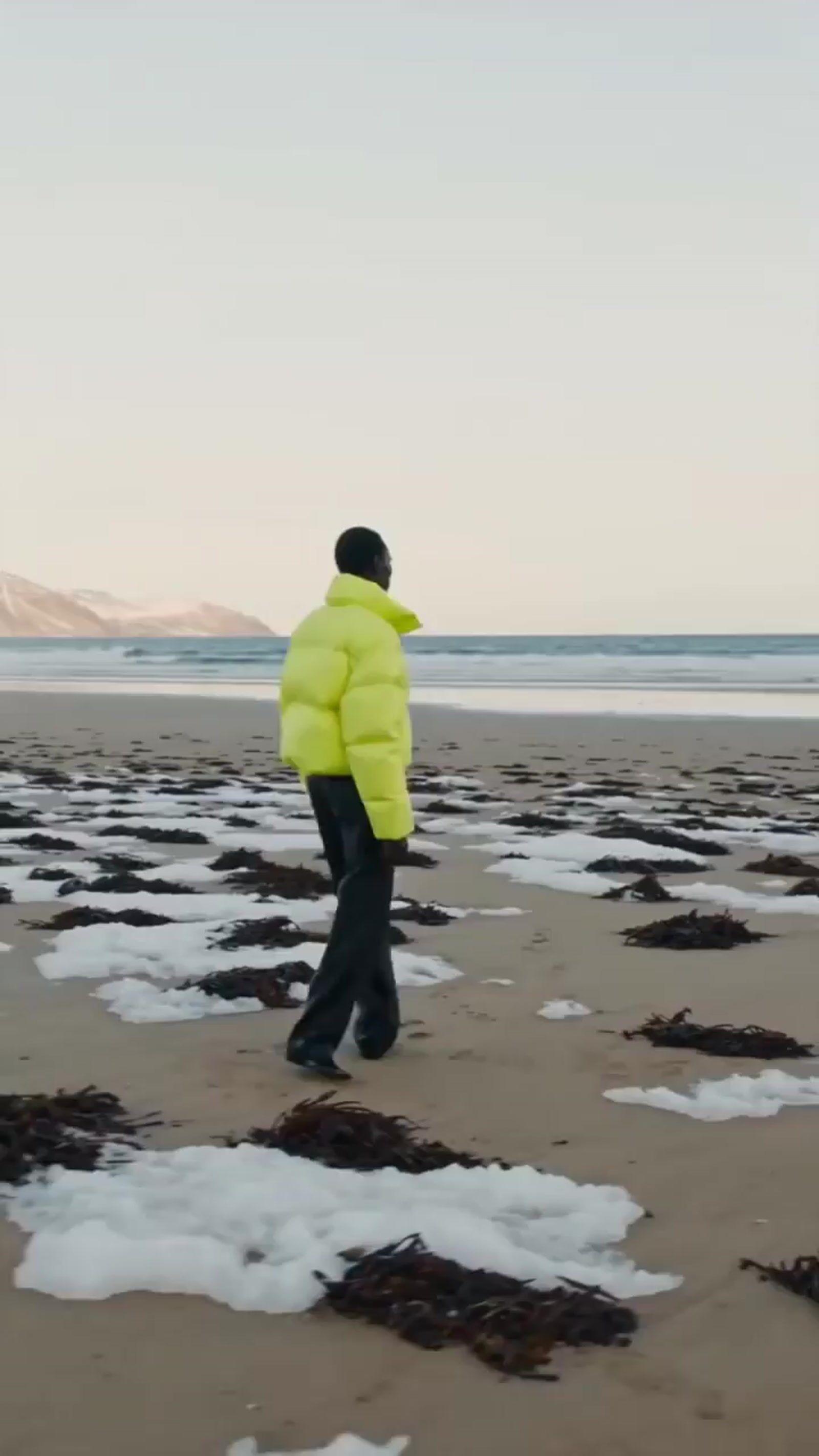 a man in a yellow jacket walking on a beach