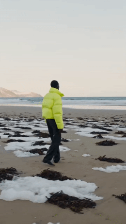 a man in a yellow jacket walking on a beach