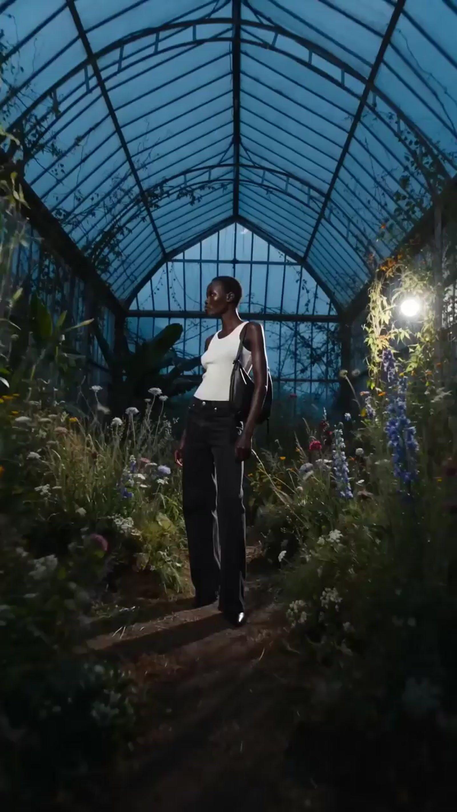 a woman in a white top and black pants standing in a greenhouse