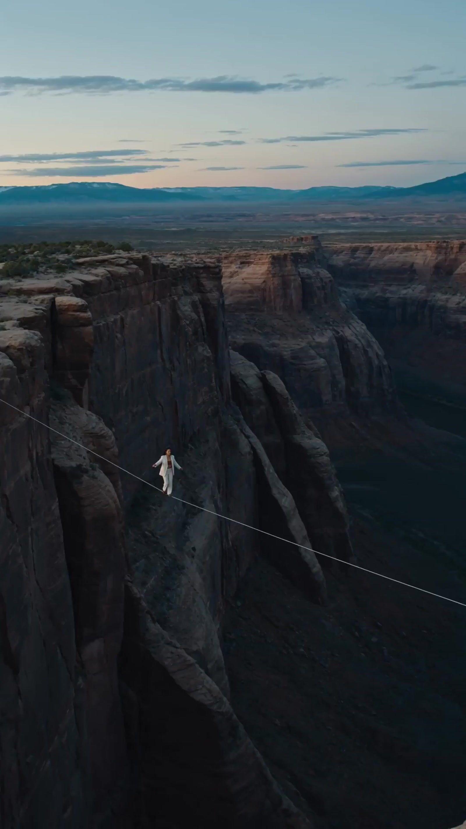 a man walking across a rope over a canyon