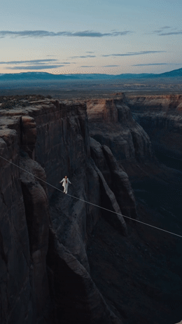 a man walking across a rope over a canyon